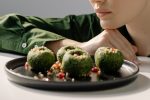 Close-up of spinach pkhali, a Georgian vegan dish, with a woman in green observing.