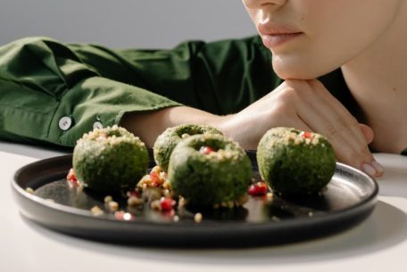Close-up of spinach pkhali, a Georgian vegan dish, with a woman in green observing.