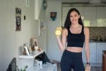 Smiling woman in activewear lifting dumbbells at home for a healthy lifestyle.